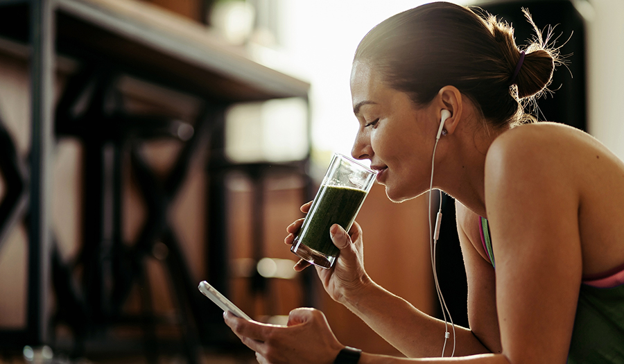 Woman drinking green juice with chlorophyll while looking at her phone