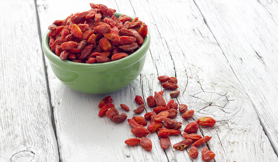 Red goji berries in green bowl on wooden table