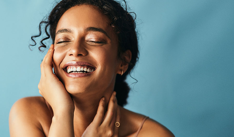 woman with hydrated, glowy skin touching her face and smiling with eyes closed