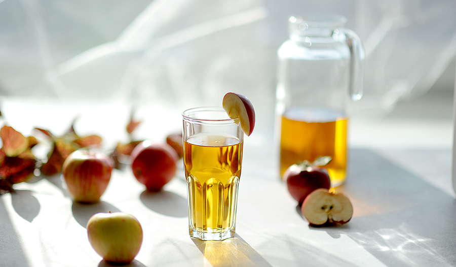 Apple cider vinegar wellness shot in glass on white background with apples and pitcher.