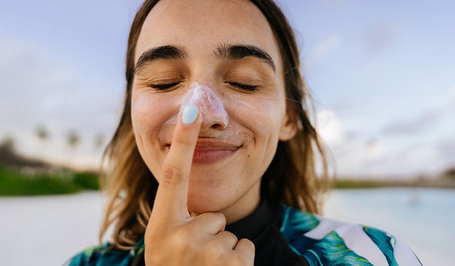 woman applying sunscreen to her nose by the beach