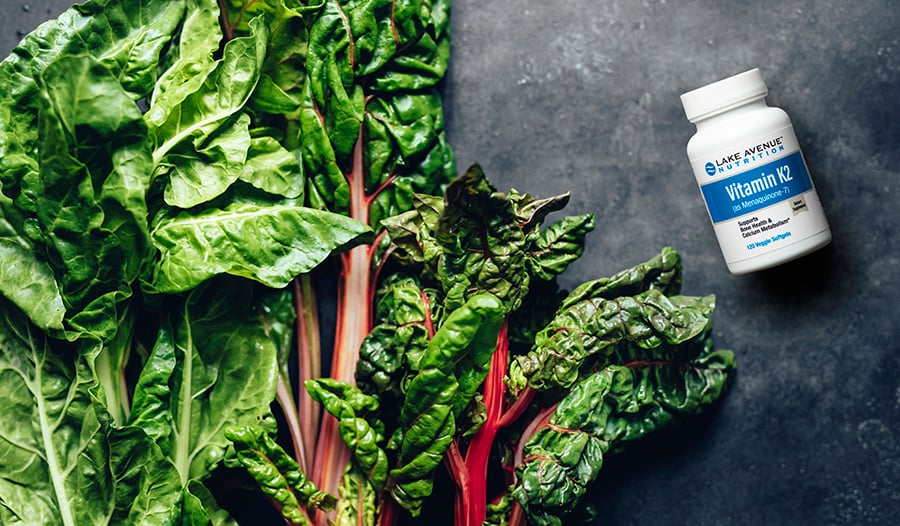 Vitamin K supplement bottle and leafy greens on concrete table