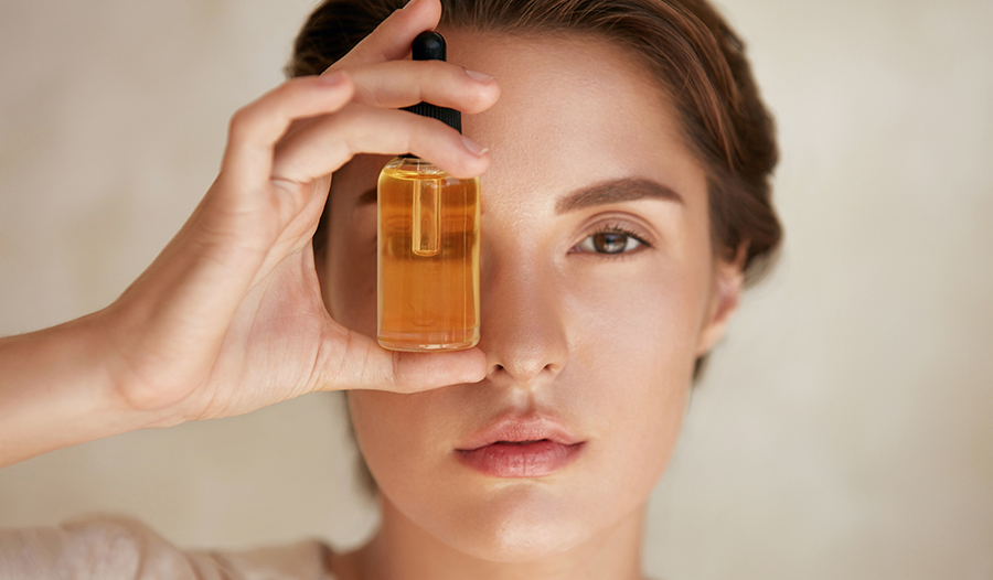 woman holding up a vitamin serum to her eye and looking through the glass bottle