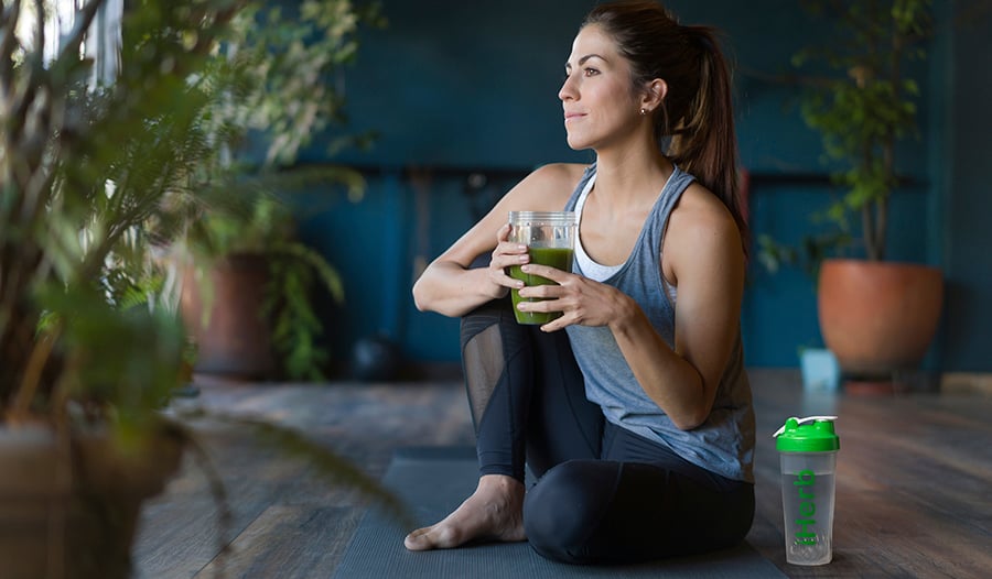 Serene woman drinking green smoothie outside on yoga mat