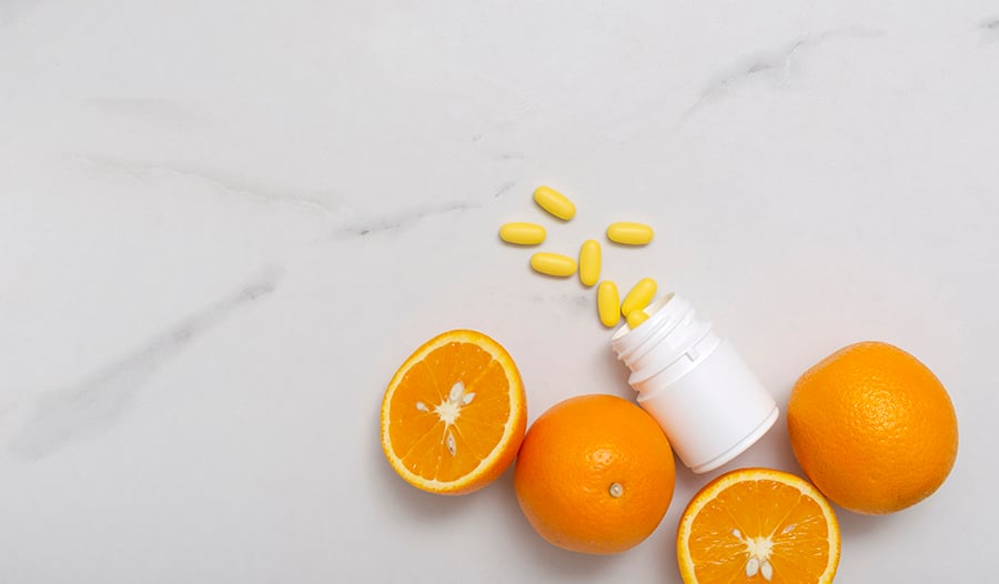 Vitamin C supplement bottle and vitamins on table with oranges