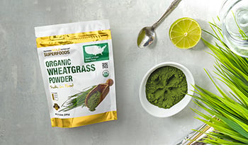 Powdered wheatgrass supplement on table with spoon, lime, and grass 
