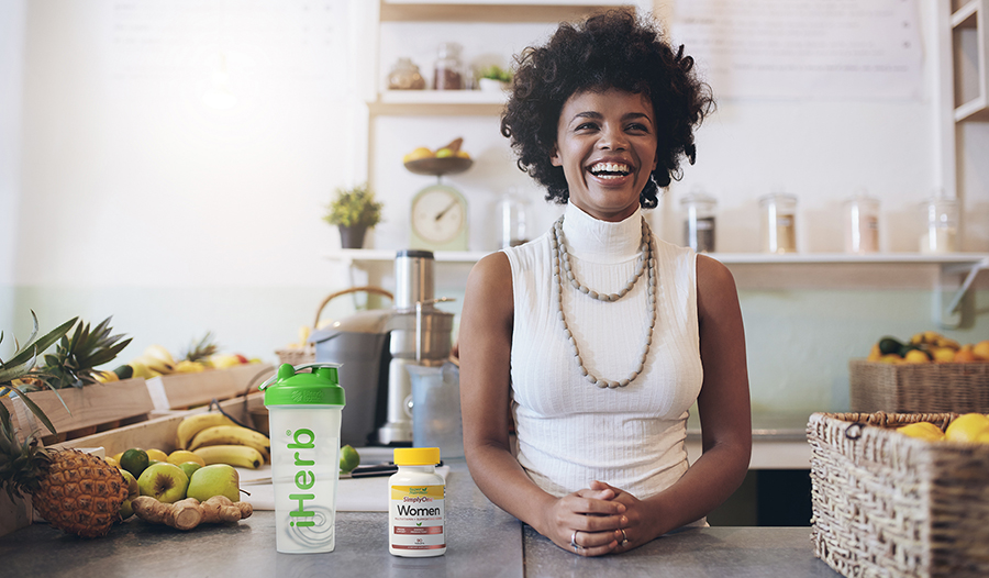 Healthy woman smiling in kitchen with fruit, water bottle, and multivitamin on counter