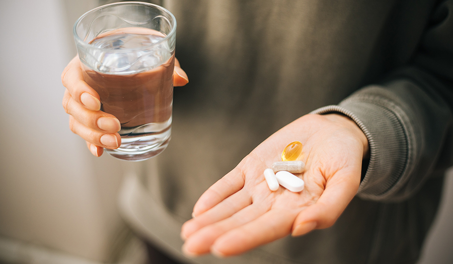 Hand with fish oil, probiotics, zinc, and other vitamins or supplements in it with glass of water