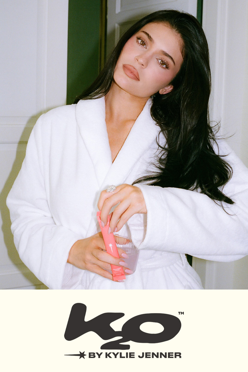 k2o by Kylie Jenner beauty hydration banner showing a woman in a white robe holding a pink stick pack and water bottle, with the K2O logo.